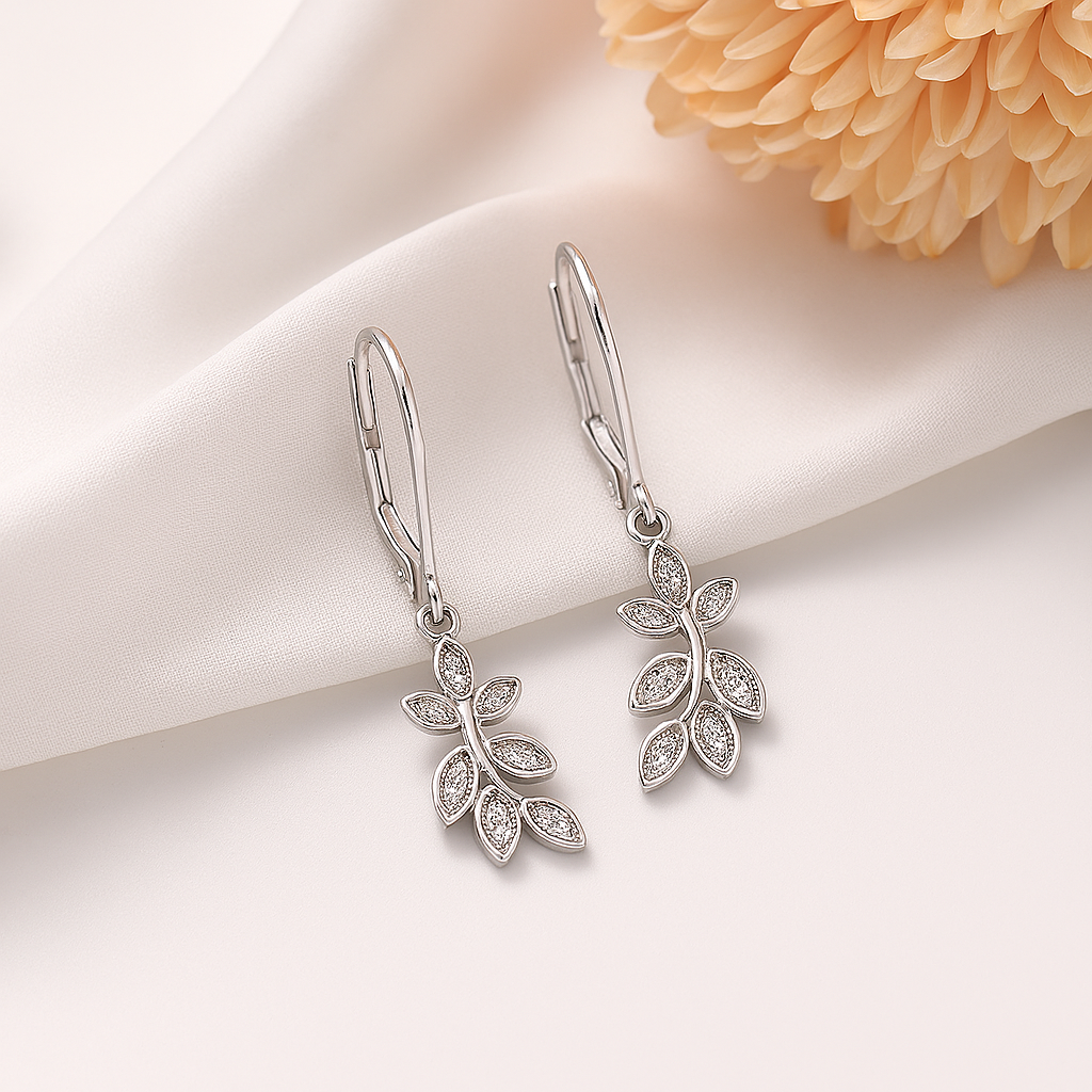 Silver leaf-shaped earrings on a soft fabric background with a flower.